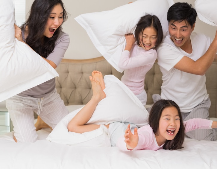 Family of four having pillow fight on bed