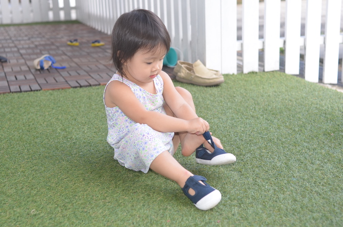 little girl tying her shoe at singapore preschool between two trees early learning school