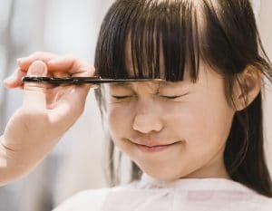 Asian girl having her forelock cut by beautician.