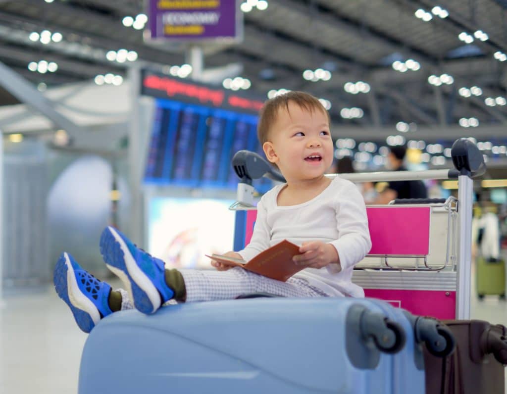 Little traveler, Cute Asian 18 months / 1 year old toddler boy child holding passport with suitcase, sitting on trolley at airport
