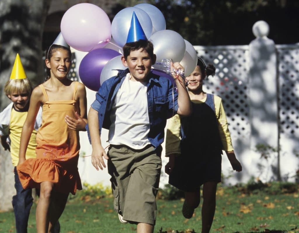 Girls and boys (7-10) playing in garden with party hats and balloons