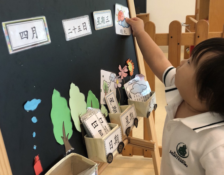 a little boy adjusts the calendar at raffles montessori kindergarten aljunied