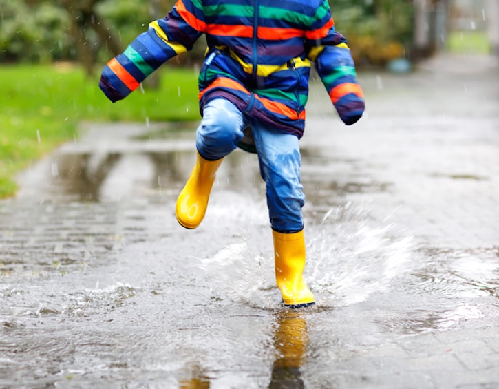 Close-up of kid wearing yellow rain boots and walking during sleet, rain and snow on cold day