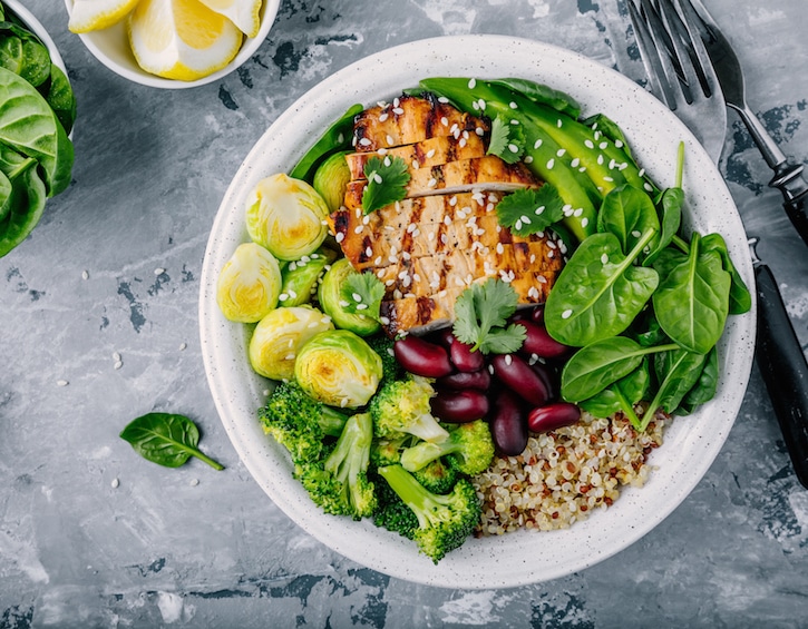 Healthy buddha bowl lunch with grilled chicken, quinoa, spinach, avocado, brussels sprouts, broccoli, red beans with sesame seeds