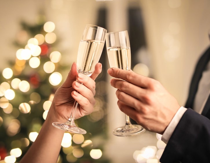 Detail of two hands toasting with wine glasses, in front of a Christmas tree