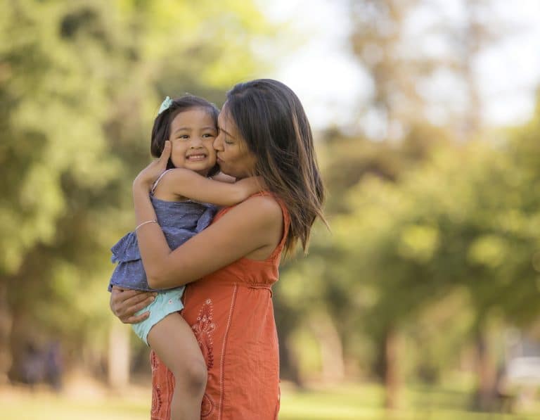 Young ethnic mother embracing her toddler girl outdoors
