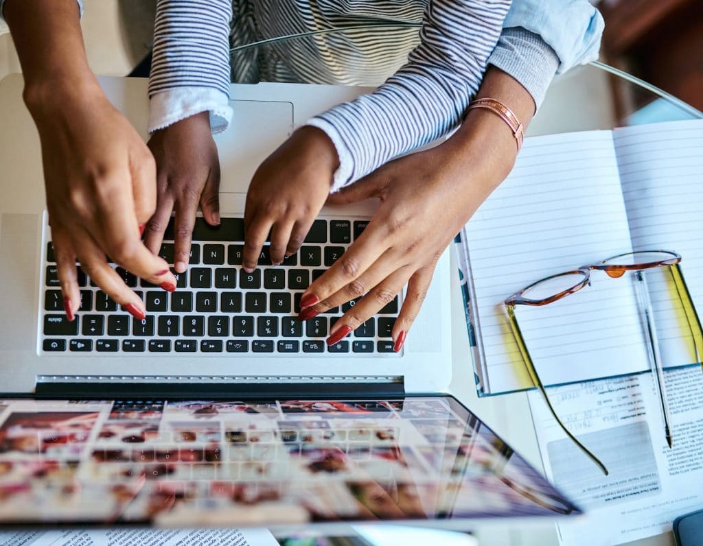 a mother types on a laptop keyboard with help from her child