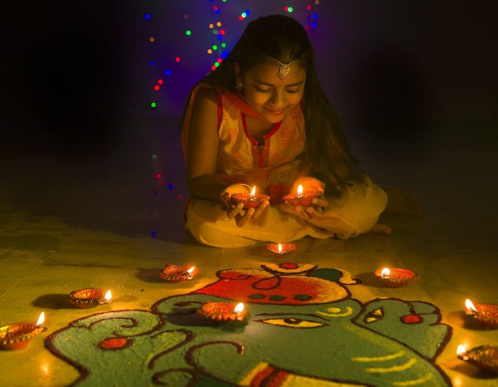 Girl making Rangoli and decorating with oil lamps for Deepavali