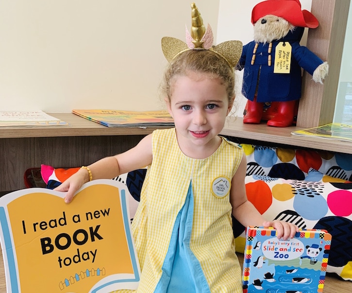 little girl reading a book in the library at the little skool house preschool 