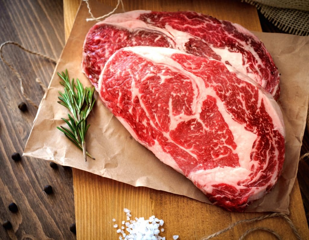 Two raw rib eye steak on a wooden Board on a table prepared for the grill. Top view rustic style