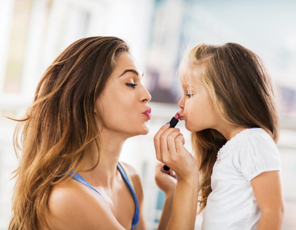 Young mother applying lipstick on her daughter.