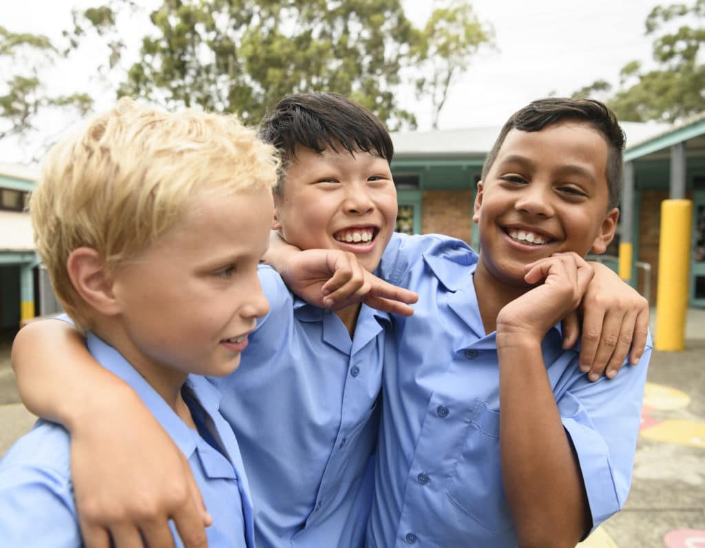 Candid portrait of three boys in school playground with arms around each other