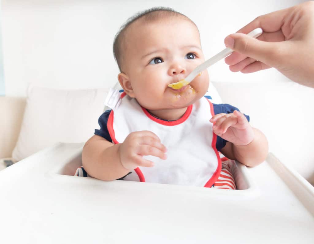 Mother feeding baby food on high chair