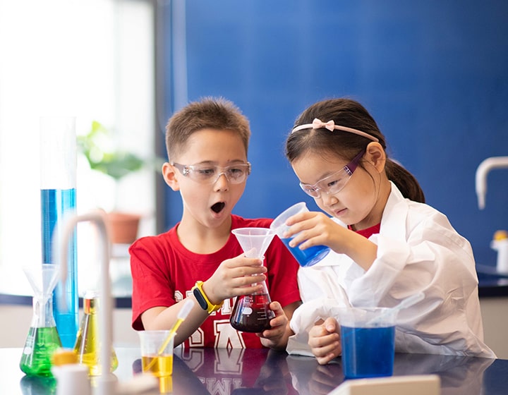 Summer Camps Singapore: Camp Asia. Two students pouring blue liquid into a flask.