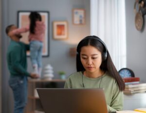 wfh mum singapore problems - mother working on laptop with headphones on with child and spouse in the background